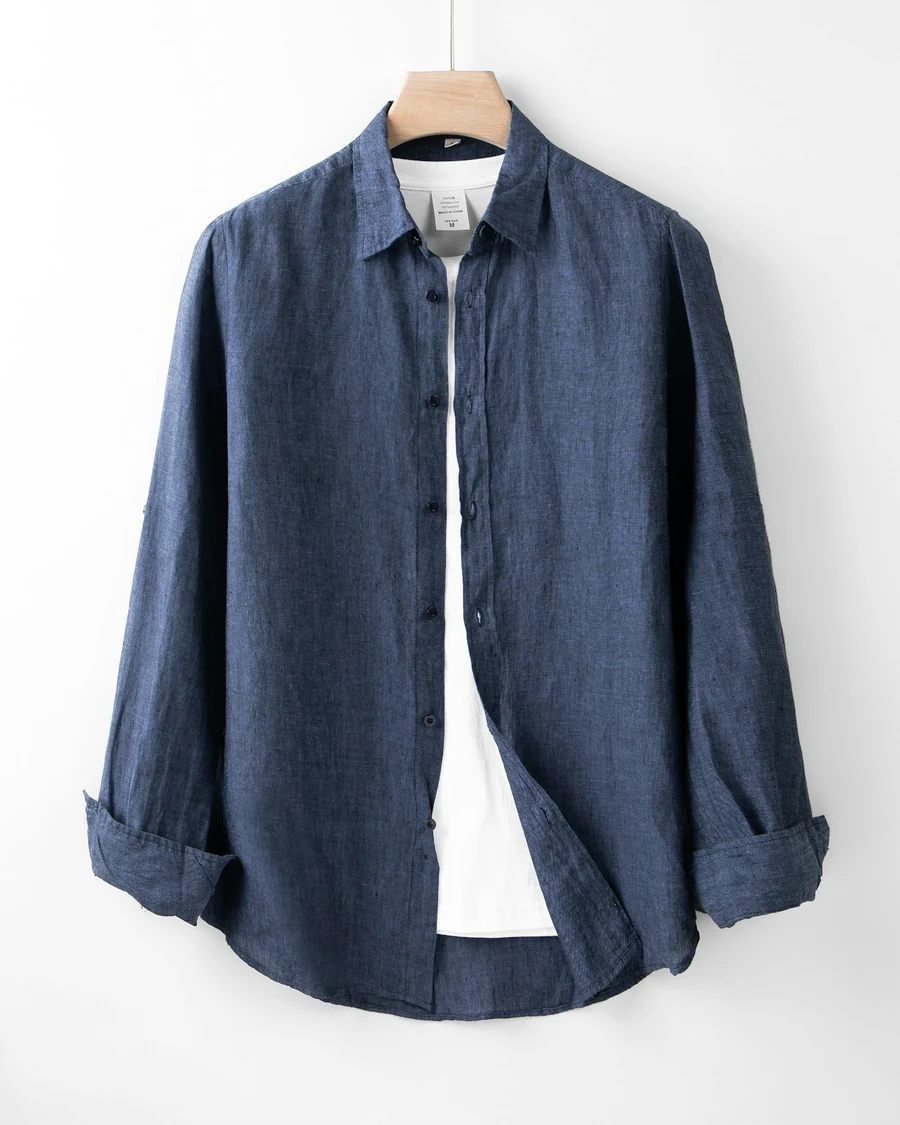 A navy long-sleeved linen shirt with rolled cuffs hanging against a white wall