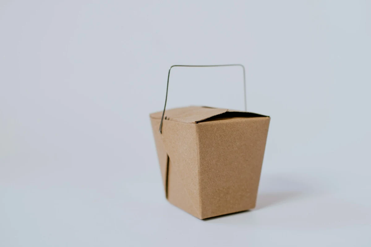 Caja de cartón marrón con asa para llevar, sobre fondo claro
