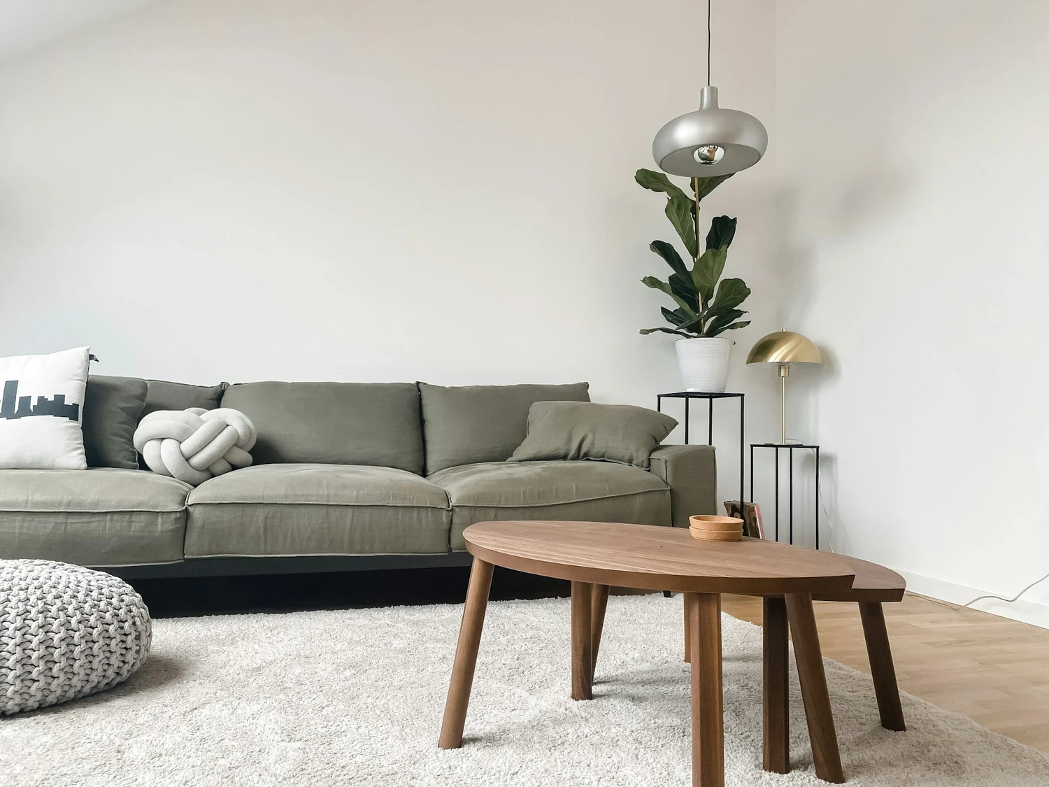 Oliwkowa sofa z lnu w jasnym salonie, drewniany stolik kawowy i biały dywan