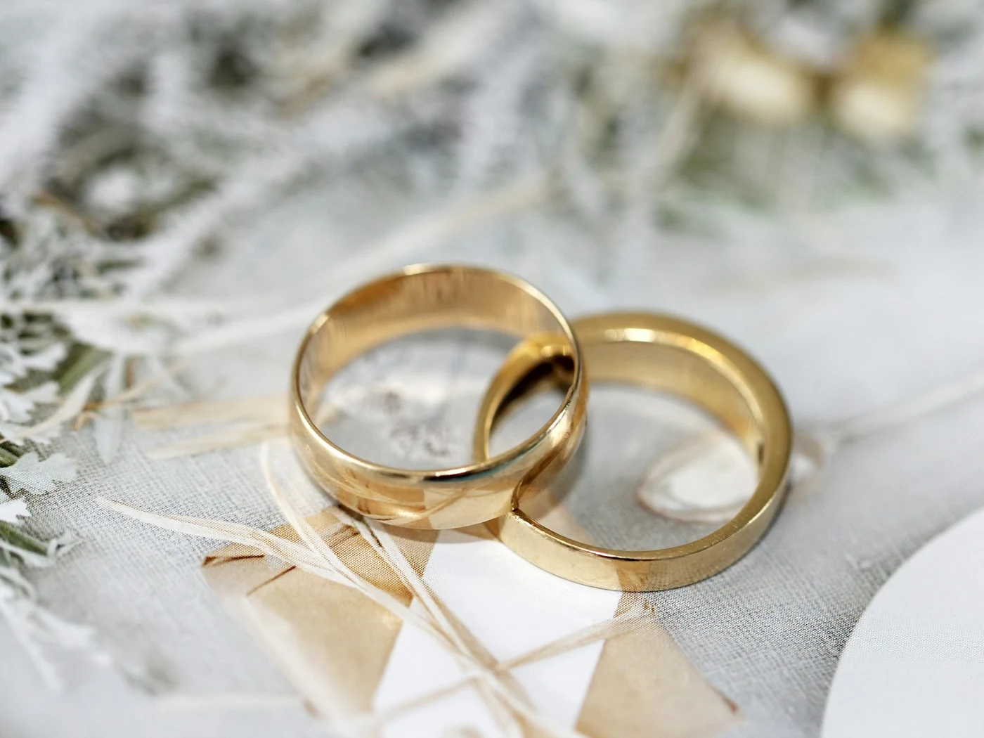 Two yellow-gold wedding bands on pale linen with dried flowers