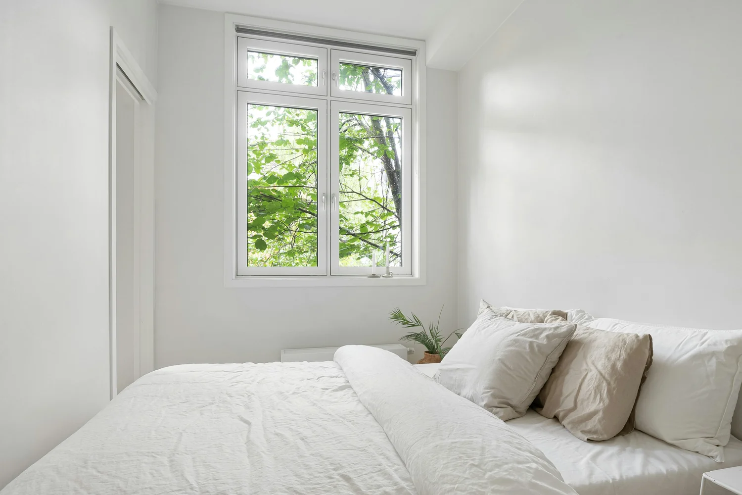 Helles Schlafzimmer mit Fenster zum Hof, draußen grünes Laub