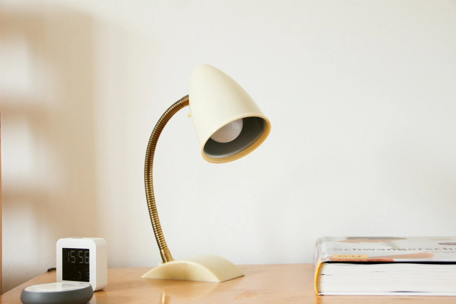 Cremefarbene Schreibtischlampe mit Messingarm auf einem Holztisch