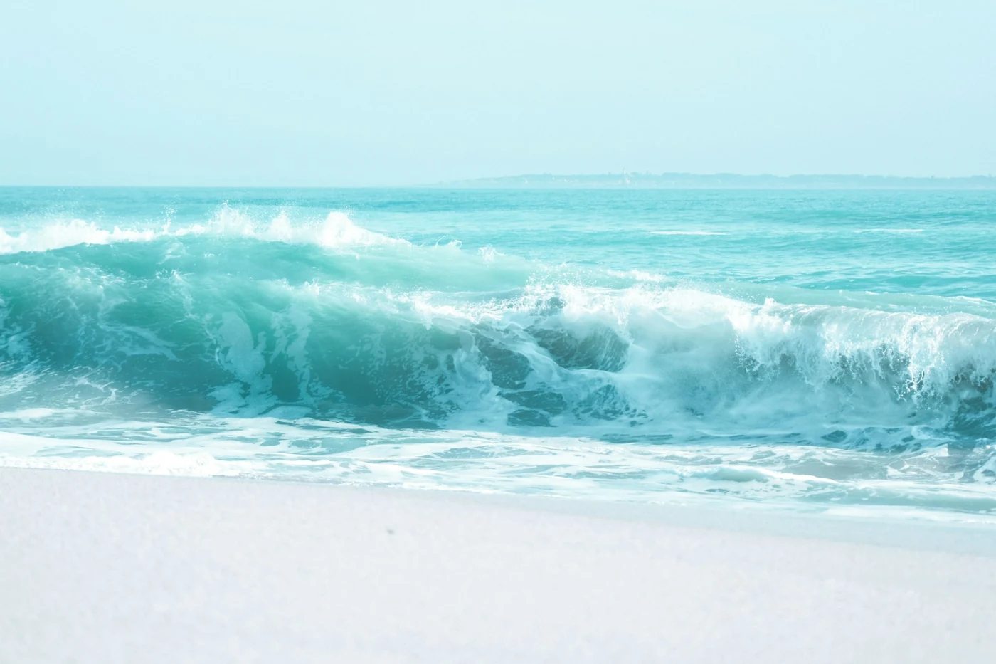 Una ola turquesa rompiendo en una playa de arena blanca