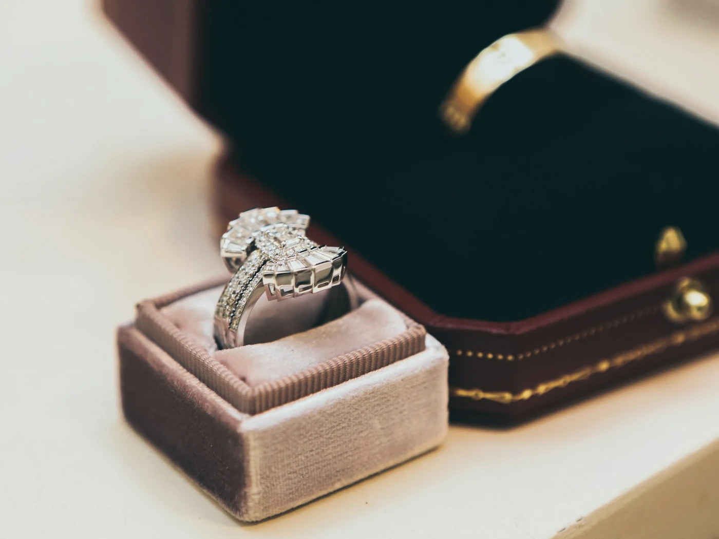Two ring boxes: a dusty-pink velvet one holding a diamond ring and an open burgundy one with a gold band