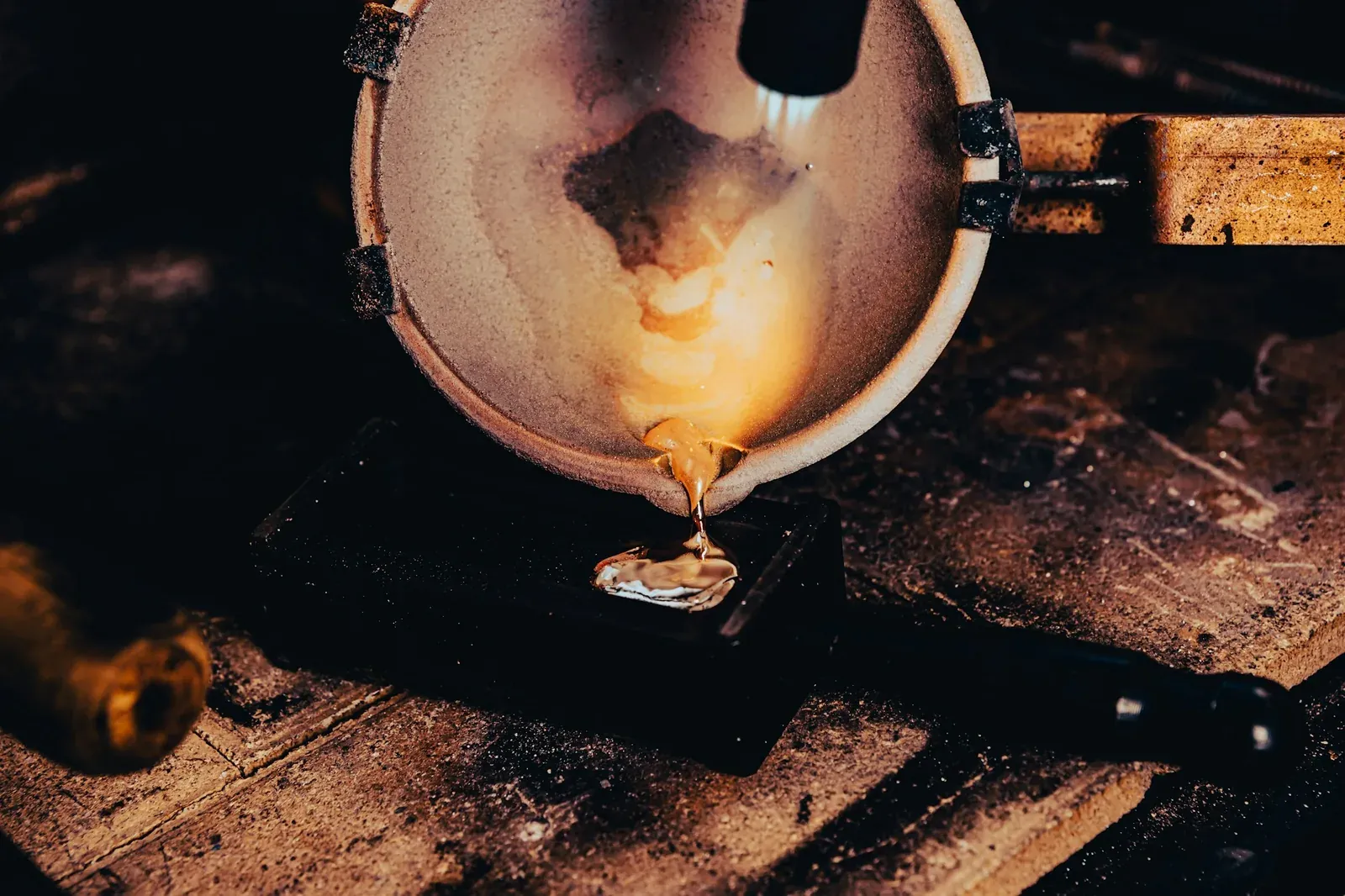 A ceramic crucible tipped over a steel block, a thin stream of molten metal running out