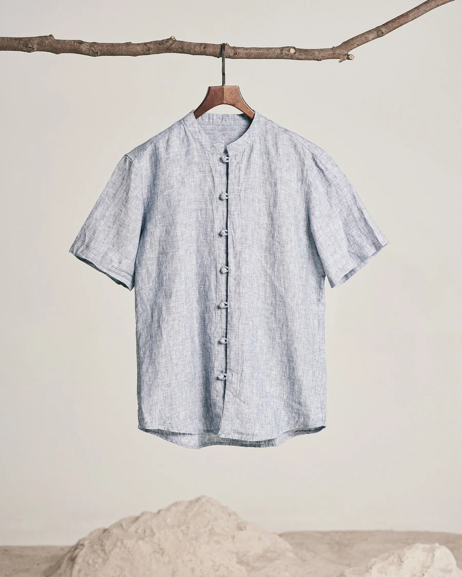 A mist-blue short-sleeved linen shirt with a band collar hanging from a branch
