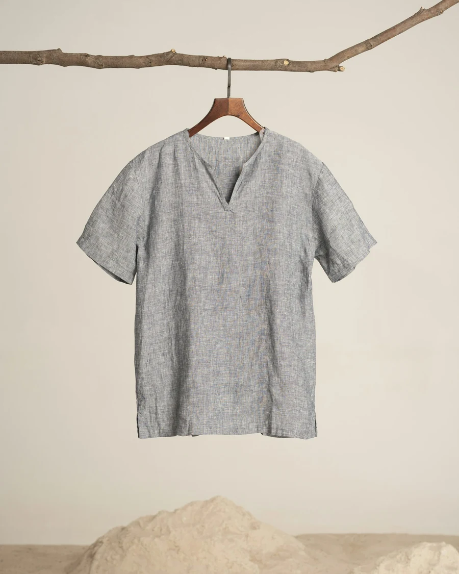 A stone-grey flecked linen shirt with a notched neckline hanging from a branch