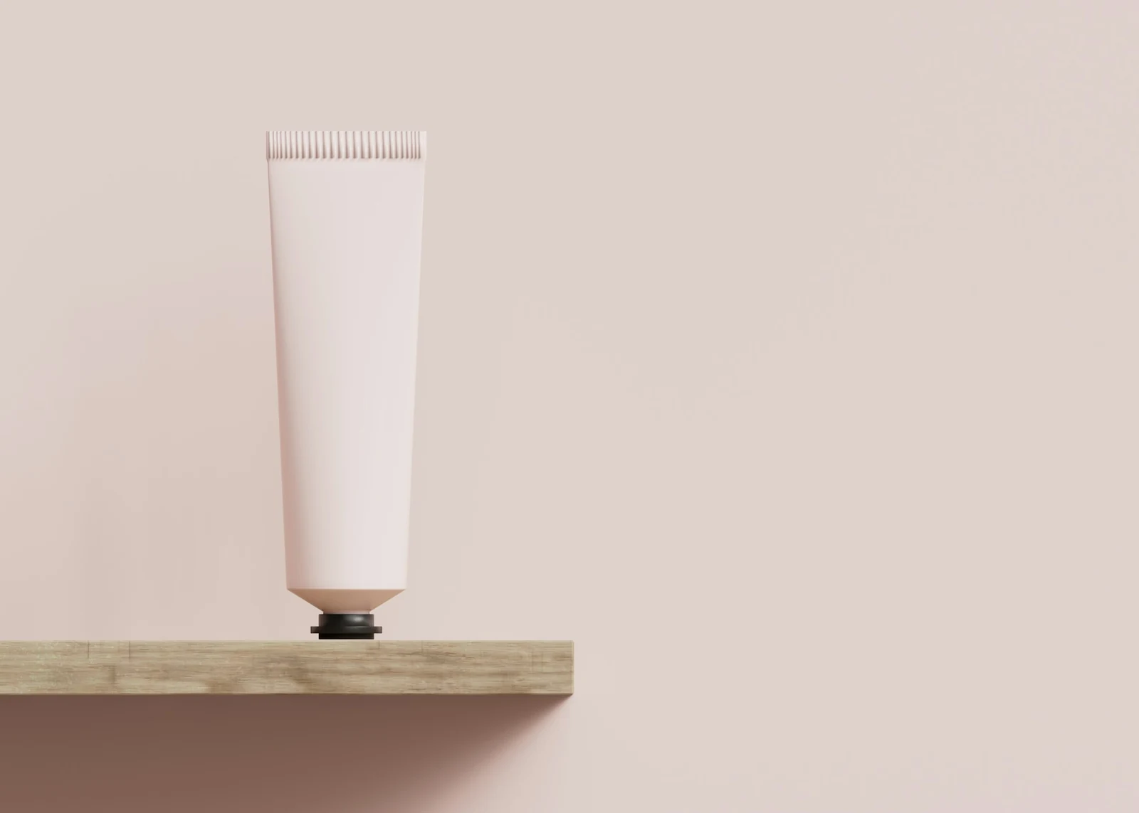 Un tubo de crema rosa pálido sobre una balda de madera, frente a una pared rosa empolvada