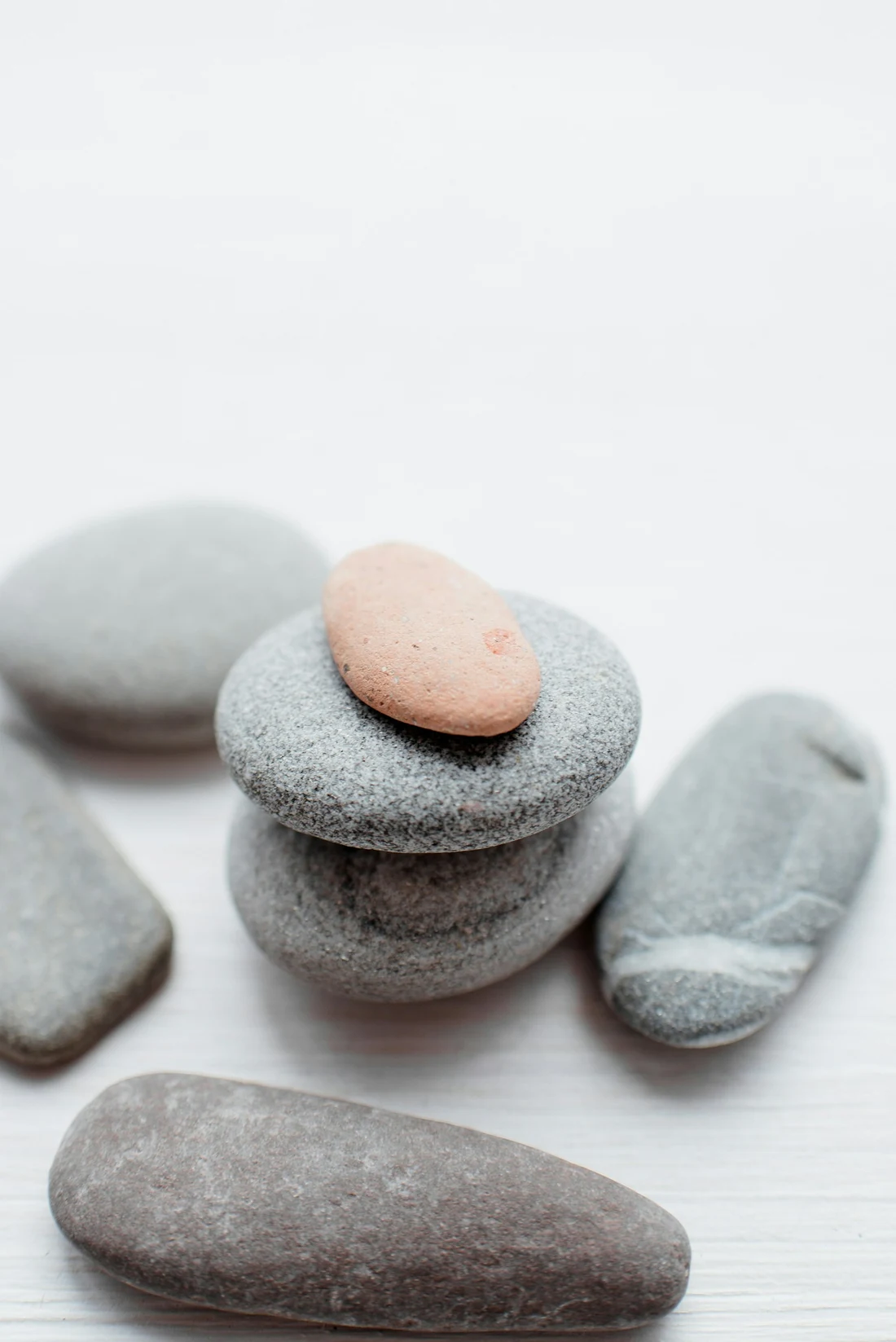 Piedras lisas grises y rosadas apiladas sobre una superficie blanca