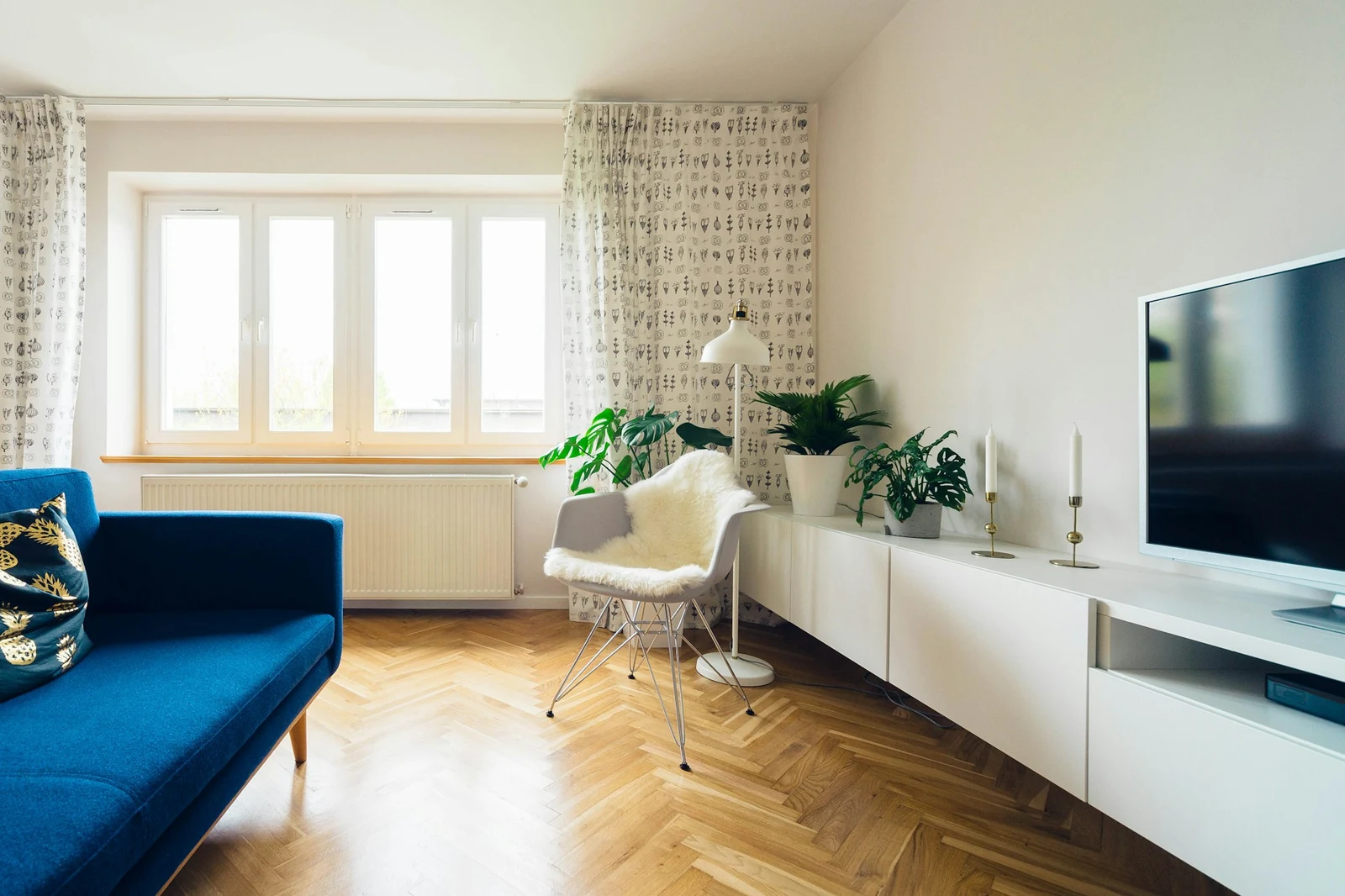 Jasny salon po remoncie: parkiet w jodełkę, niebieska sofa, okna i biała szafka pod telewizor