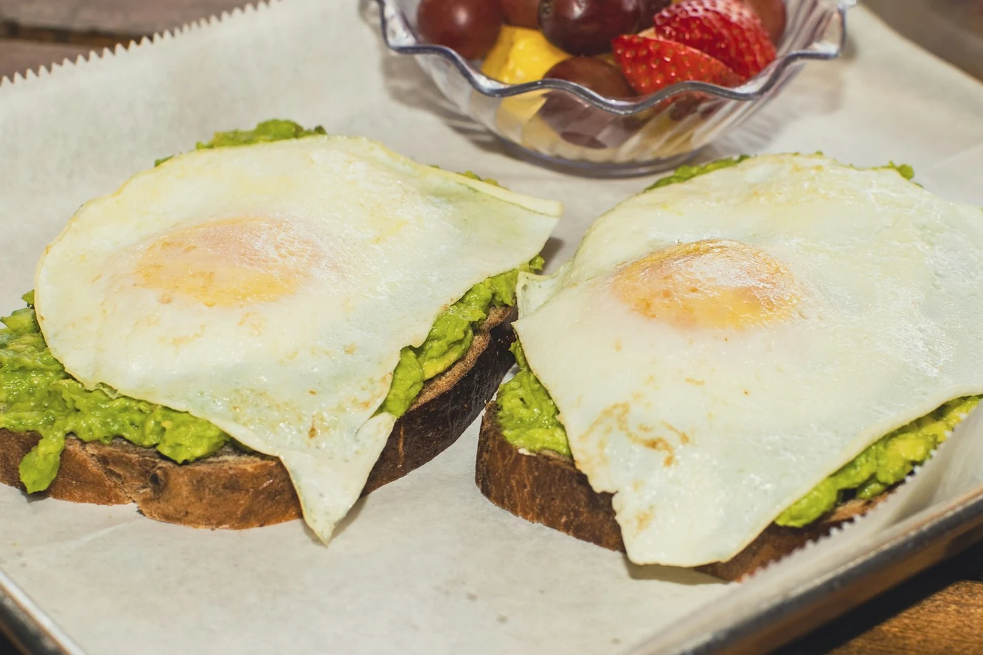 Dos tostadas con aguacate y huevo frito sobre papel de horno