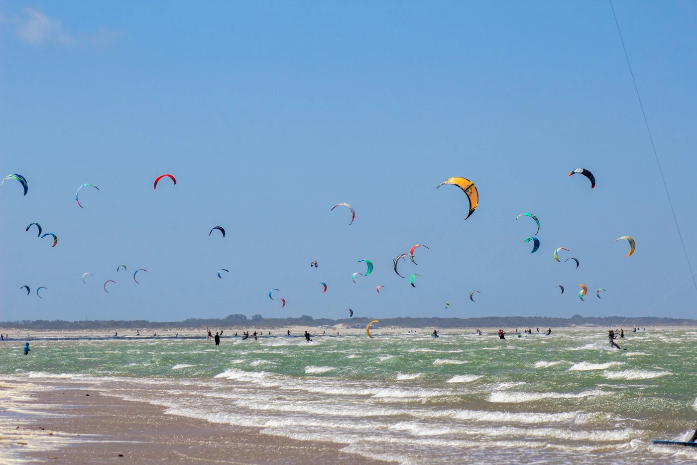 Muchos kites de colores en el cielo azul sobre una playa de arena