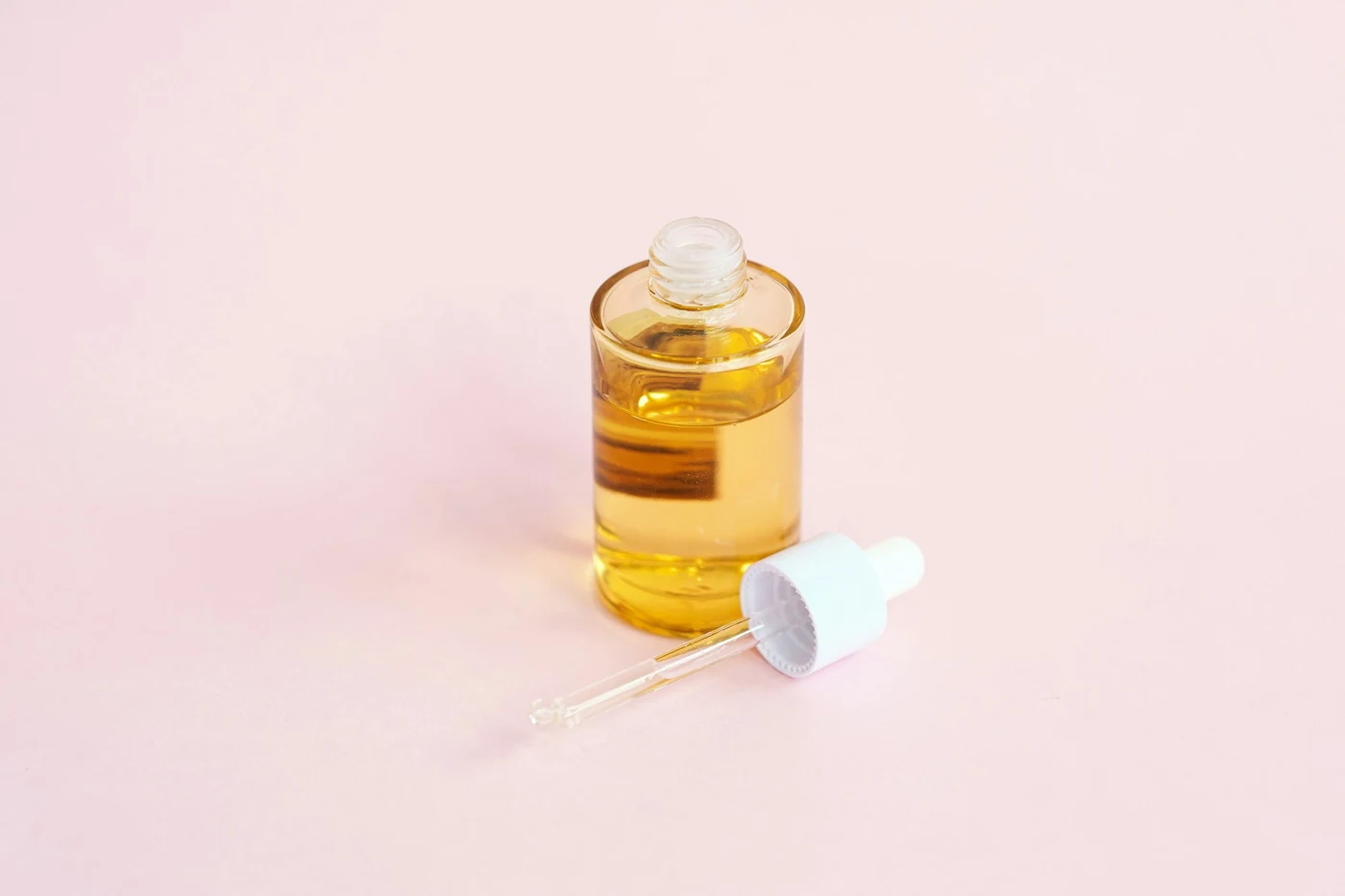 Frasco de sérum con gotero y su tapa sobre una superficie rosa suave
