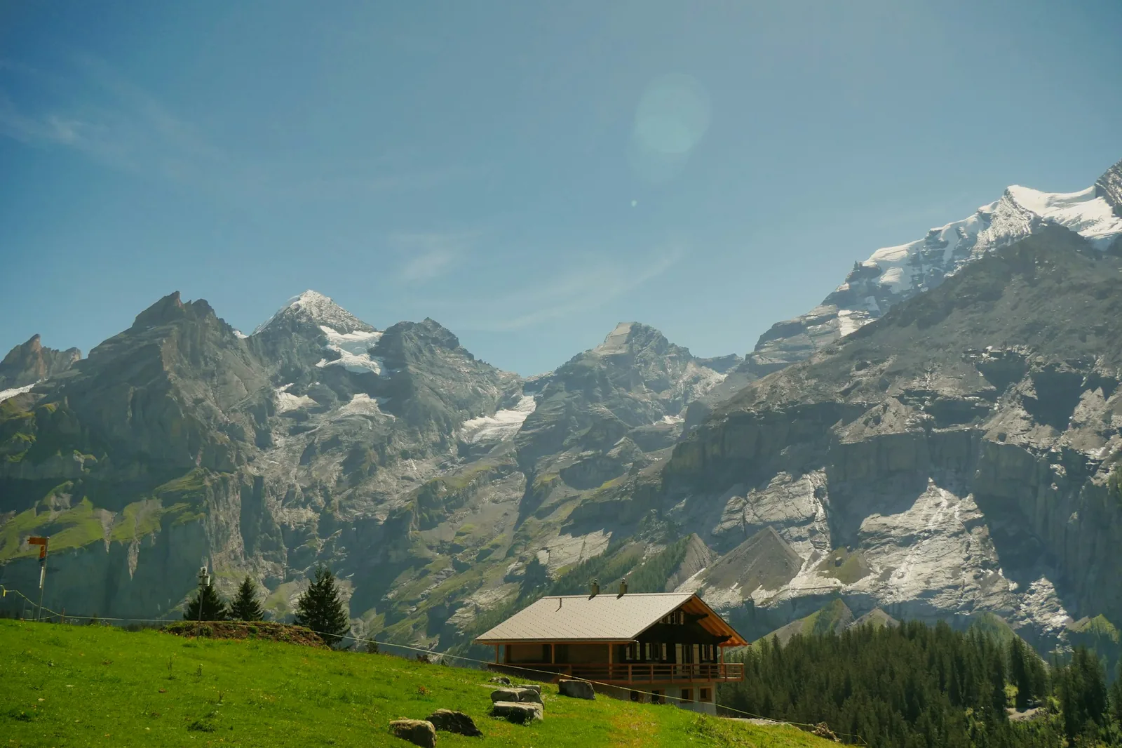 Holzhütte auf einer grünen Alpenwiese unter schneebedeckten Gipfeln